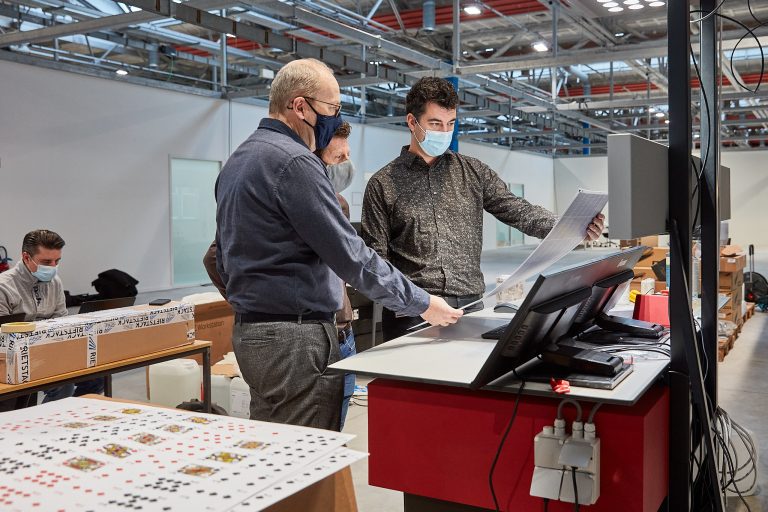 3 engineers on a machine with a sheet of playing cards